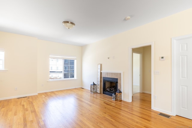 unfurnished living room featuring light wood-type flooring, a tiled fireplace, and visible vents