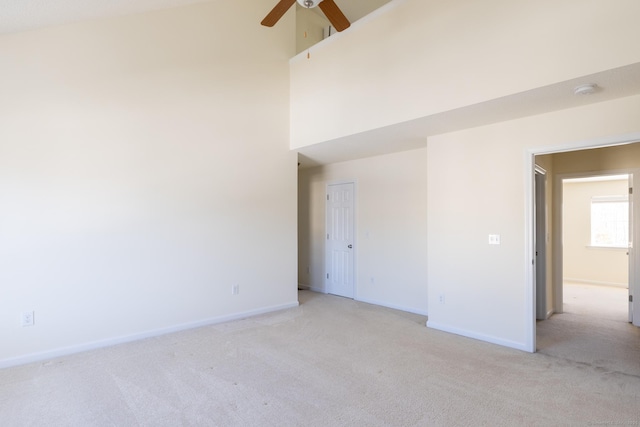 unfurnished room featuring a towering ceiling, baseboards, a ceiling fan, and light colored carpet