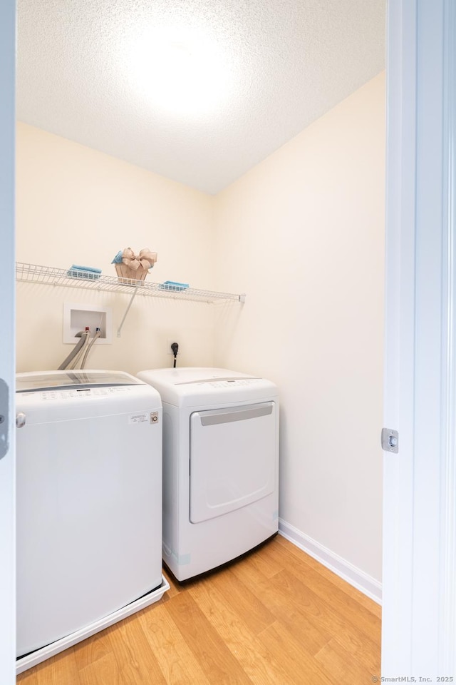 laundry area with laundry area, baseboards, wood finished floors, a textured ceiling, and washer and dryer