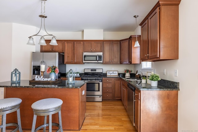 kitchen featuring appliances with stainless steel finishes, brown cabinetry, hanging light fixtures, and light wood-style flooring