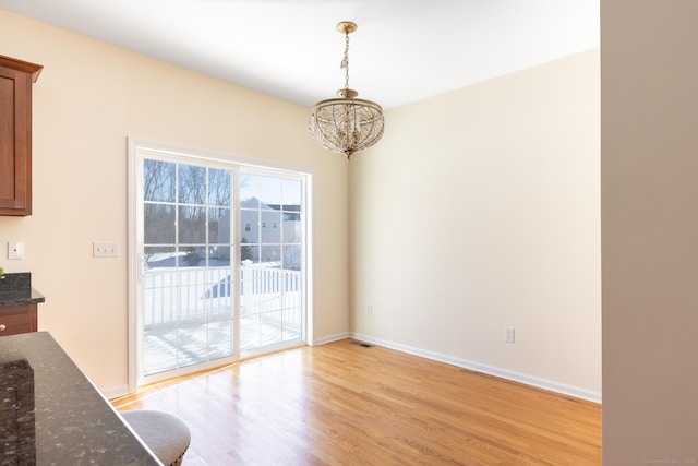 unfurnished dining area featuring a notable chandelier, light wood-type flooring, and baseboards