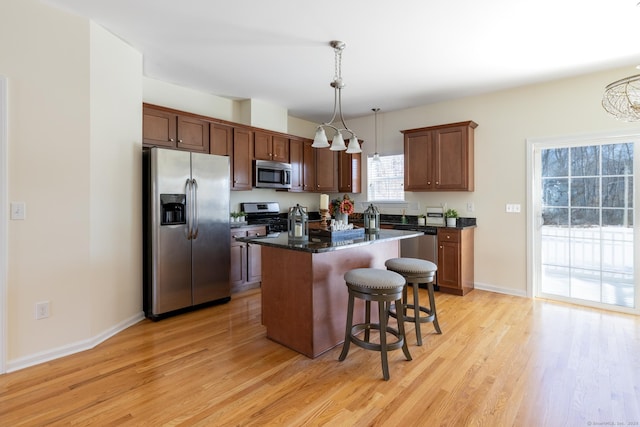 kitchen with light wood-type flooring, appliances with stainless steel finishes, pendant lighting, and a center island