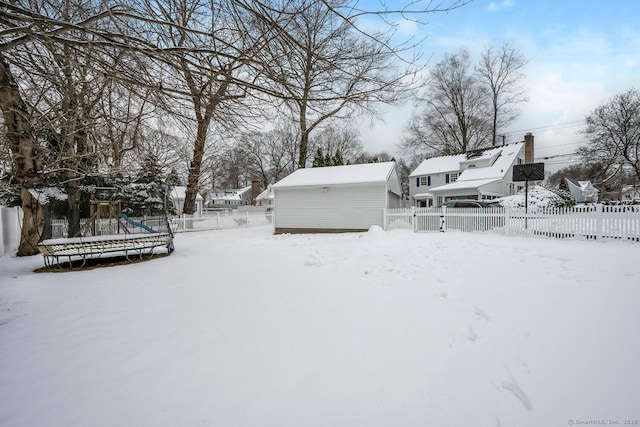 yard covered in snow with an outbuilding, a playground, and a trampoline