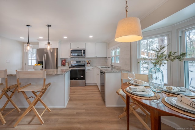 kitchen featuring a sink, backsplash, white cabinetry, light wood-style floors, and appliances with stainless steel finishes