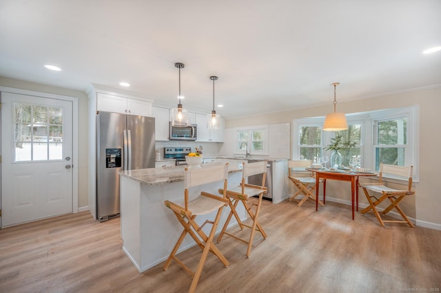 kitchen featuring light wood finished floors, a center island, light stone counters, appliances with stainless steel finishes, and white cabinetry