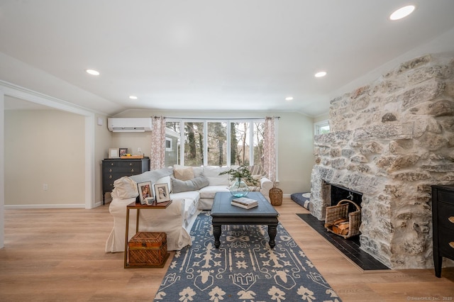 living area with baseboards, a fireplace, vaulted ceiling, a wall mounted air conditioner, and light wood-type flooring