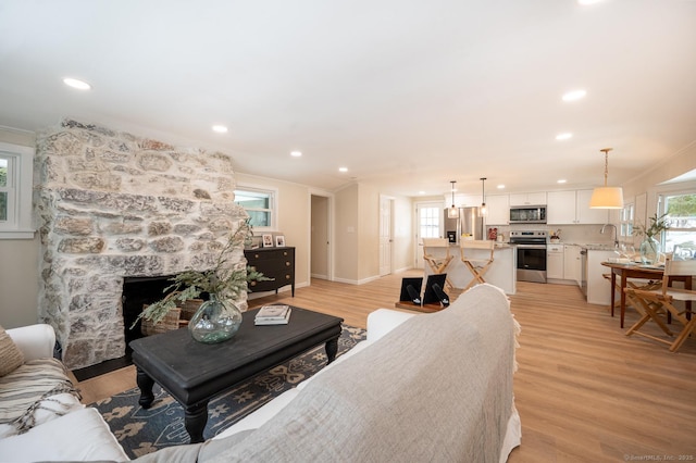 living room featuring baseboards, recessed lighting, ornamental molding, a stone fireplace, and light wood-type flooring