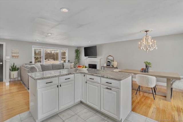 kitchen with white cabinetry, decorative light fixtures, light stone countertops, and light hardwood / wood-style floors