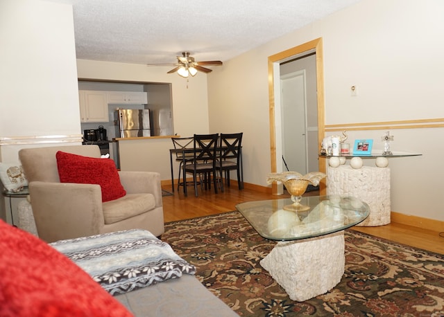 living room featuring hardwood / wood-style flooring, ceiling fan, and a textured ceiling