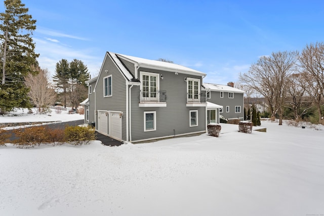 snow covered back of property with a garage and a balcony