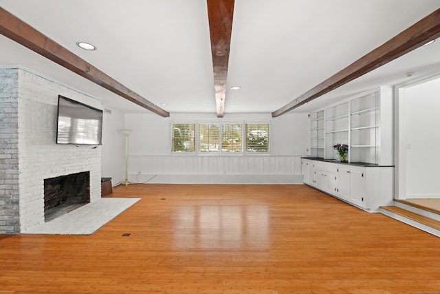 unfurnished living room featuring a brick fireplace, beam ceiling, and light hardwood / wood-style flooring