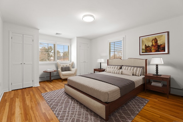 bedroom with two closets, light hardwood / wood-style flooring, and a baseboard heating unit