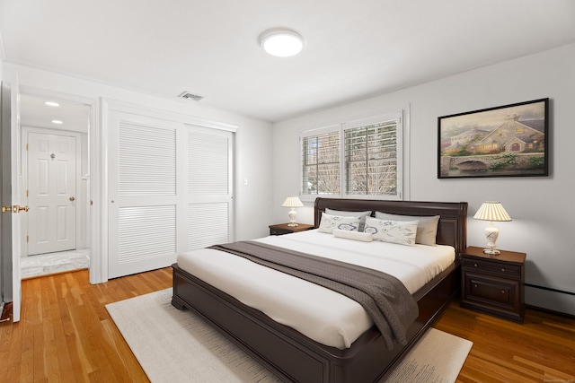 bedroom featuring baseboard heating, light wood-type flooring, and a closet