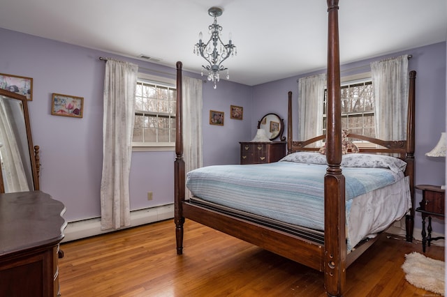 bedroom featuring an inviting chandelier, a baseboard radiator, visible vents, and wood finished floors