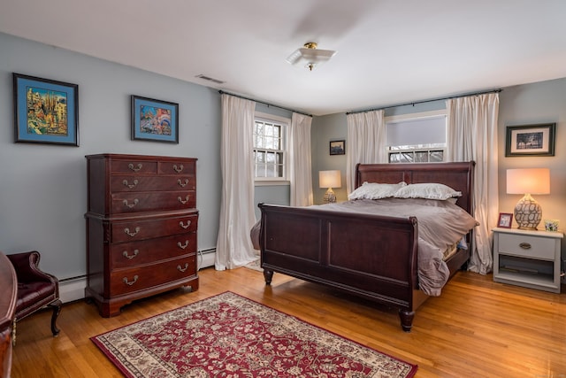 bedroom with light wood finished floors, visible vents, and a baseboard heating unit