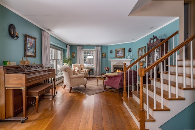 living area featuring ornamental molding, wood-type flooring, a lit fireplace, and stairs