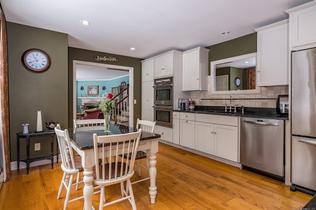 kitchen with a sink, white cabinetry, appliances with stainless steel finishes, light wood-type flooring, and a kitchen bar