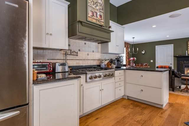 kitchen with a peninsula, appliances with stainless steel finishes, white cabinetry, and light wood-style floors