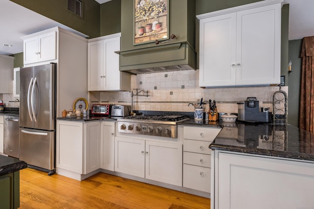 kitchen with light wood-style flooring, white cabinets, appliances with stainless steel finishes, decorative backsplash, and dark stone countertops