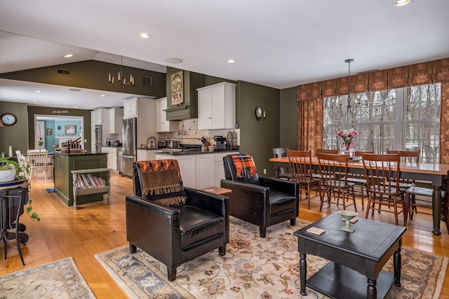 living room with vaulted ceiling, light wood finished floors, and an inviting chandelier