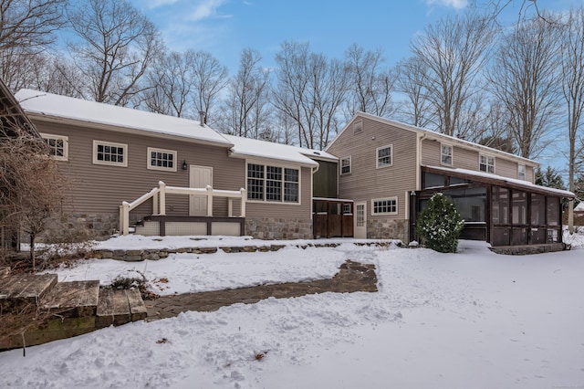 snow covered house with stone siding and a sunroom