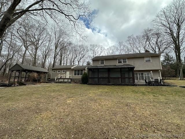 rear view of property with a sunroom, a chimney, and a yard