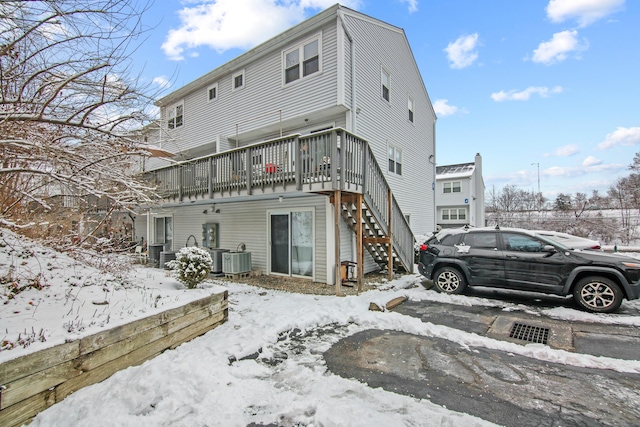 snow covered property with a deck, central AC unit, and stairs