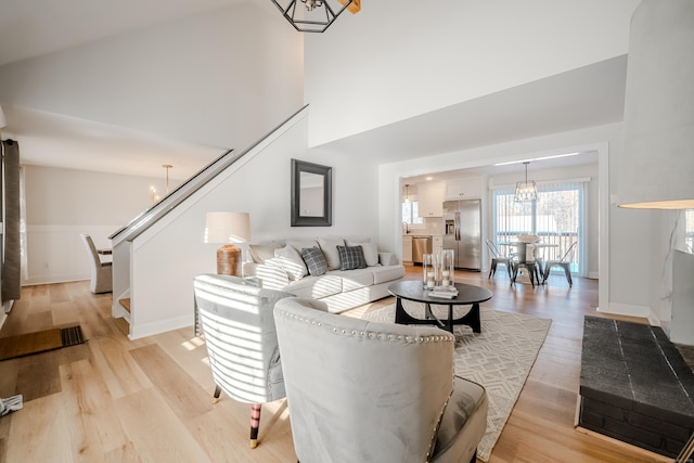 living area with stairs, a towering ceiling, light wood-style flooring, and a notable chandelier