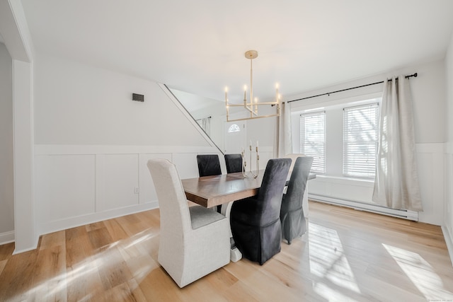 dining area featuring a chandelier, light wood-type flooring, a wainscoted wall, and baseboard heating