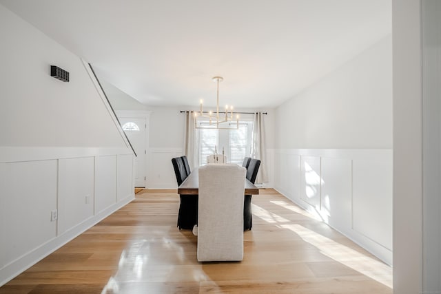 dining room with a chandelier, wainscoting, a decorative wall, and light wood-style flooring