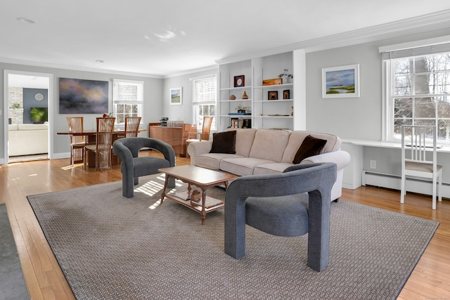 living room with light wood-type flooring, a wealth of natural light, baseboard heating, and crown molding