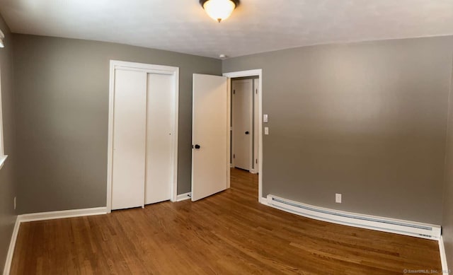 unfurnished bedroom with hardwood / wood-style flooring, a baseboard radiator, and a closet