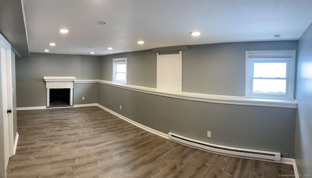 basement featuring wood-type flooring, a brick fireplace, and a baseboard heating unit