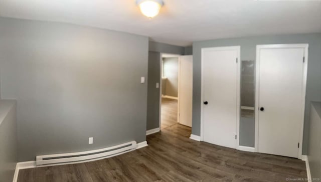 unfurnished bedroom featuring baseboard heating and dark hardwood / wood-style floors