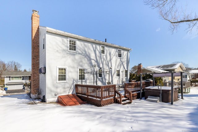 snow covered back of property with a deck, a chimney, and a hot tub