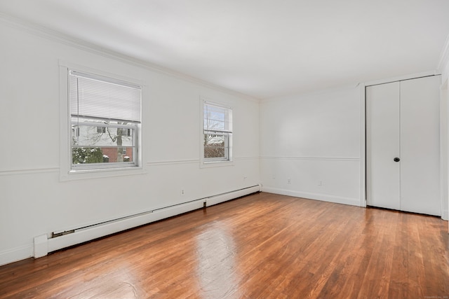 unfurnished bedroom with multiple windows, crown molding, a baseboard heating unit, and hardwood / wood-style floors