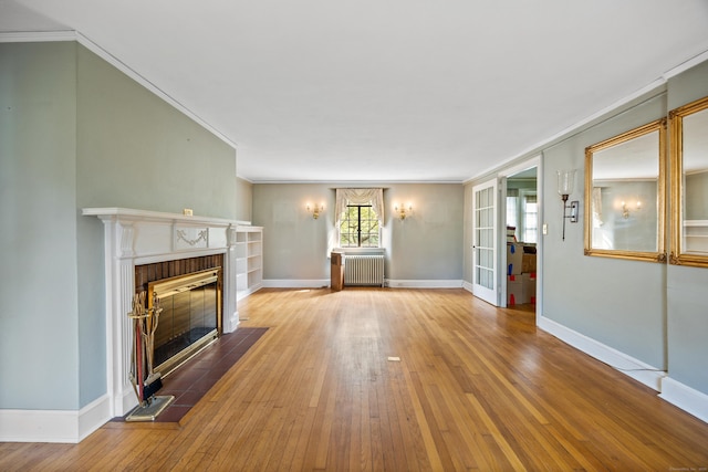 unfurnished living room featuring crown molding, a brick fireplace, radiator heating unit, and light wood-type flooring