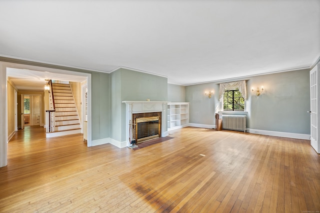 unfurnished living room with hardwood / wood-style floors, ornamental molding, a brick fireplace, and radiator heating unit