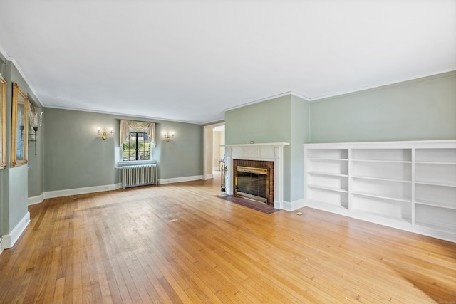 unfurnished living room featuring ornamental molding, radiator heating unit, wood-type flooring, and a brick fireplace