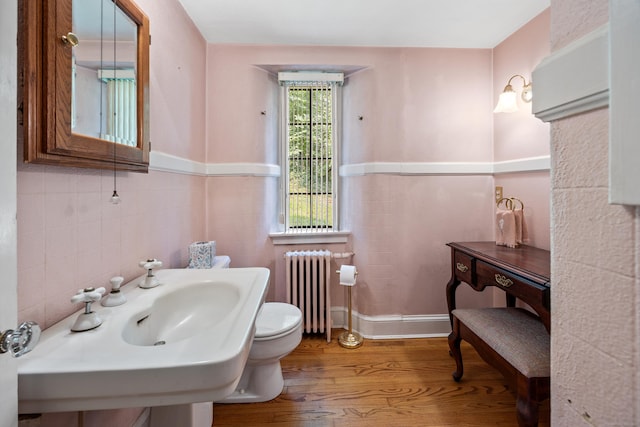 bathroom featuring radiator, sink, tile walls, hardwood / wood-style flooring, and toilet