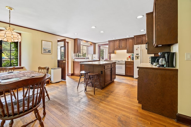 kitchen with crown molding, hanging light fixtures, a kitchen island, light hardwood / wood-style floors, and a kitchen bar