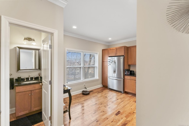 kitchen with a sink, light wood-type flooring, freestanding refrigerator, dark countertops, and crown molding