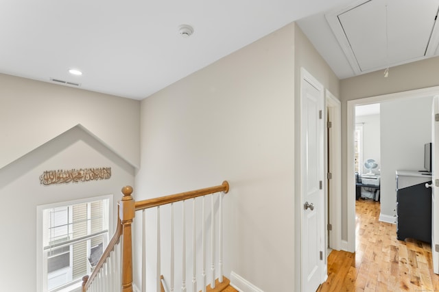 hallway with visible vents, light wood-style flooring, attic access, an upstairs landing, and baseboards