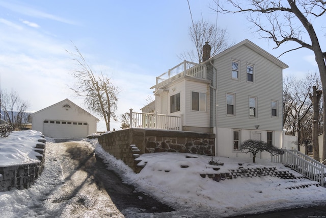 view of snowy exterior with an outbuilding, a chimney, a balcony, and a garage