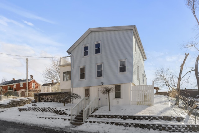 snow covered back of property featuring fence and a balcony