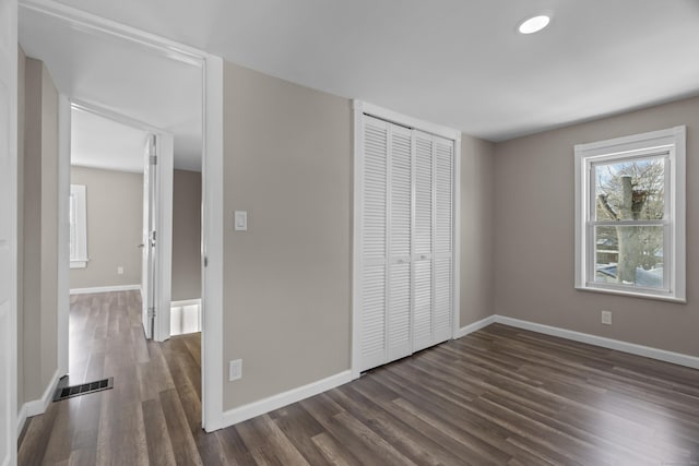 unfurnished bedroom with dark wood-style floors, a closet, visible vents, and baseboards