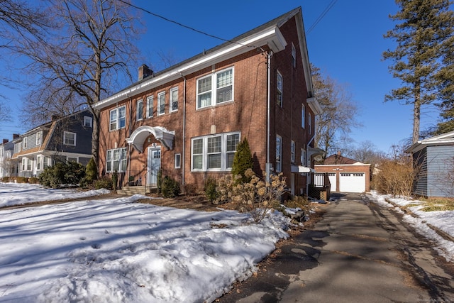 view of front of home featuring an outbuilding, brick siding, a detached garage, driveway, and a chimney