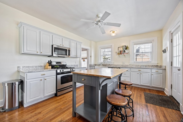 kitchen featuring a ceiling fan, white cabinetry, light wood-style floors, appliances with stainless steel finishes, and a kitchen bar