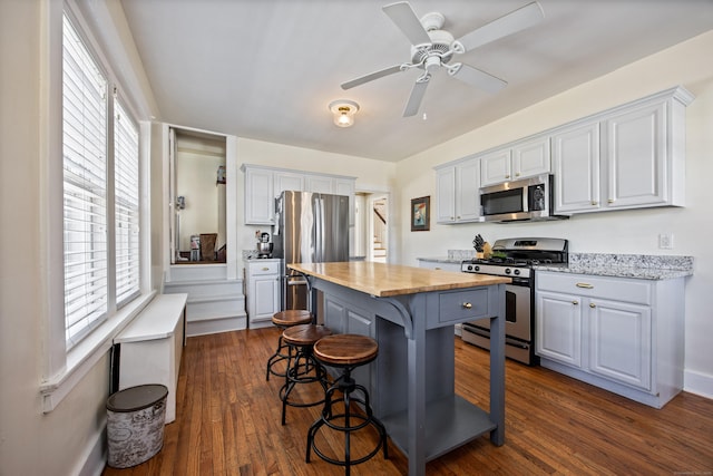 kitchen featuring dark wood-type flooring, a kitchen breakfast bar, wooden counters, appliances with stainless steel finishes, and a center island