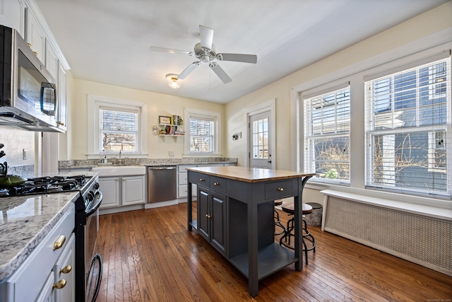 kitchen featuring white cabinets, radiator heating unit, a kitchen island, light stone counters, and stainless steel appliances